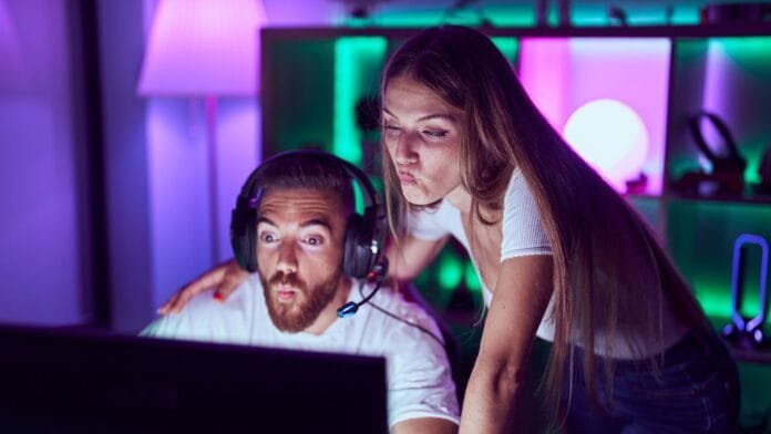Pareja jugando videojuegos en setup gaming con audífonos y luces RGB celebrando Día del Gamer Colombia 2025