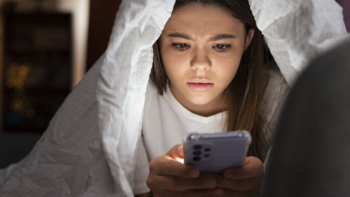 Joven usando smartphone en la cama siendo vulnerable a fraudes online relacionados con película F1 y estafas de streaming