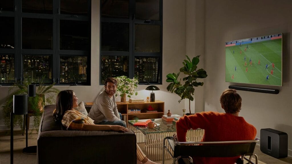 Dos personas viendo fútbol en sala con barra de sonido Sonos Beam y parlantes Era 300